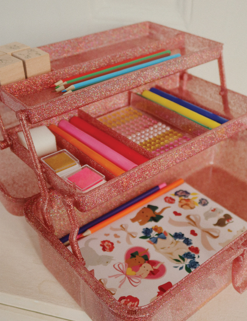 Pink glittery art supply case with stationery items on a white background