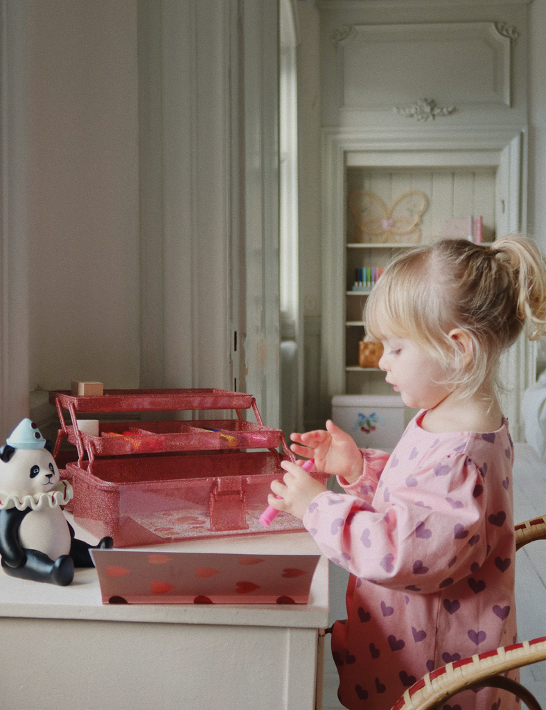 Child playing with a pink toy box in a room with white walls and furniture.