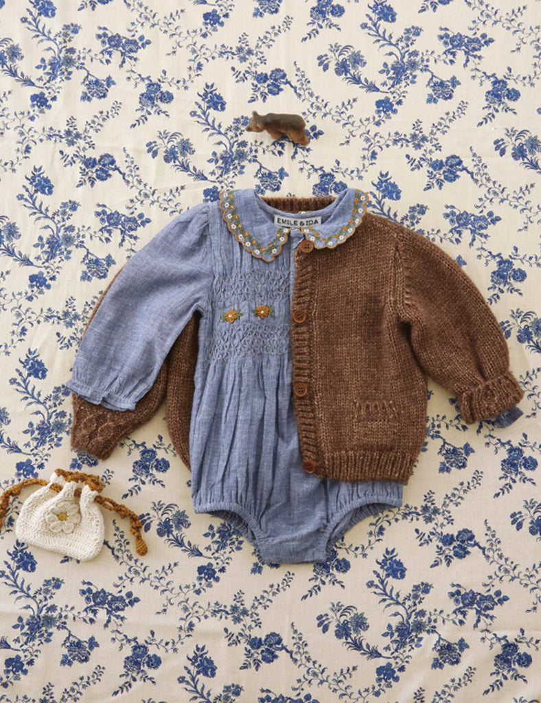 Baby outfit with blue romper and brown cardigan on a floral patterned background