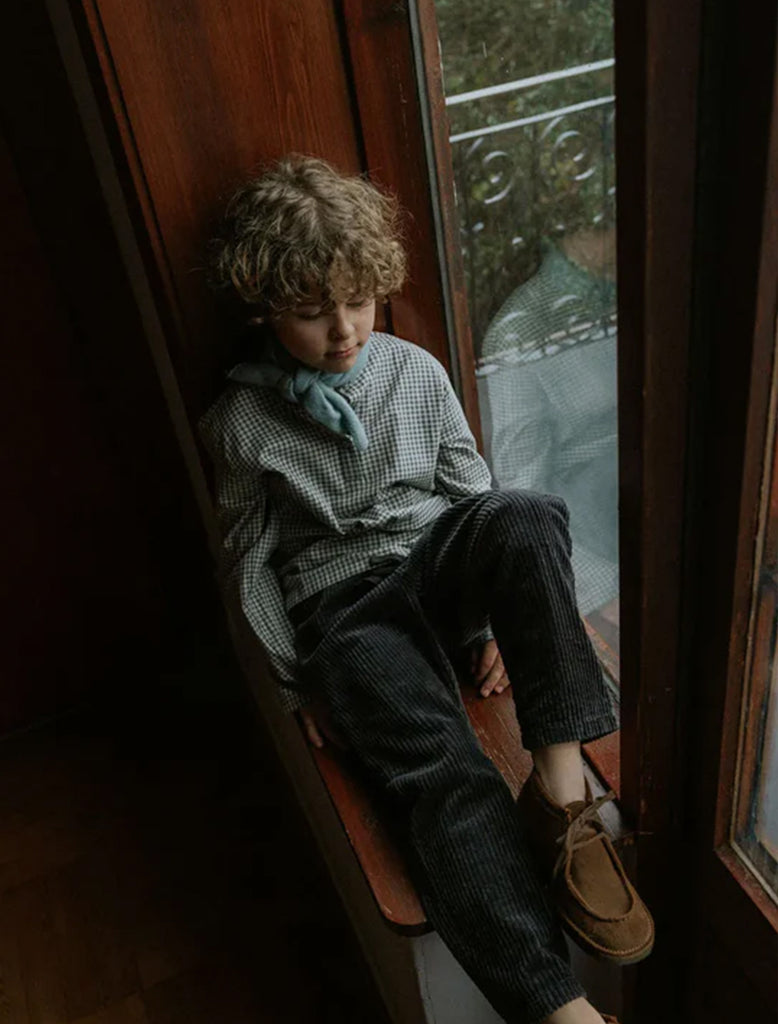 Child sitting on a window sill with a reflective surface behind
