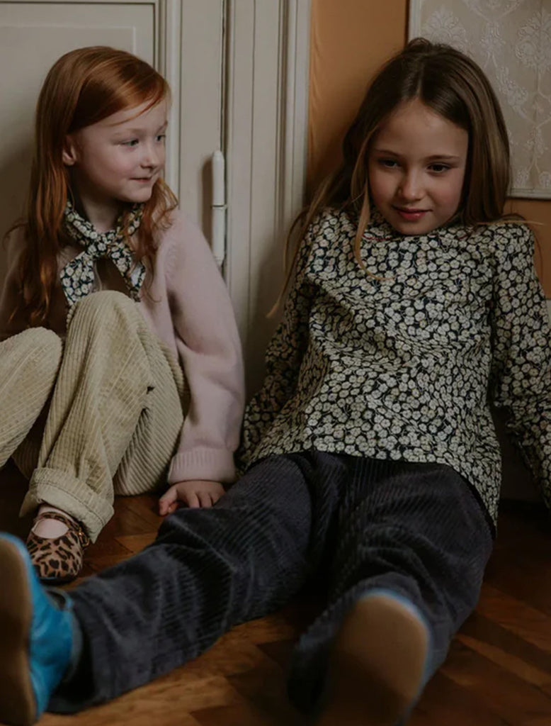 Two young girls sitting on a wooden floor, wearing patterned sweaters.