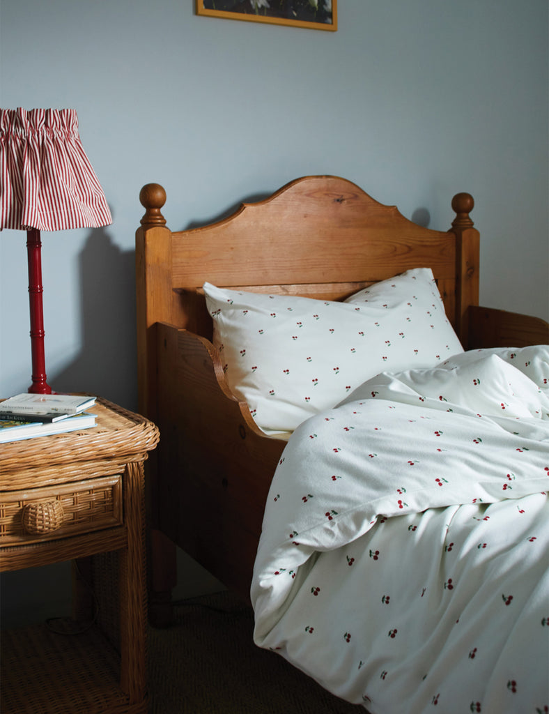 Bedroom with wooden bed and nightstand, featuring a lamp and books.