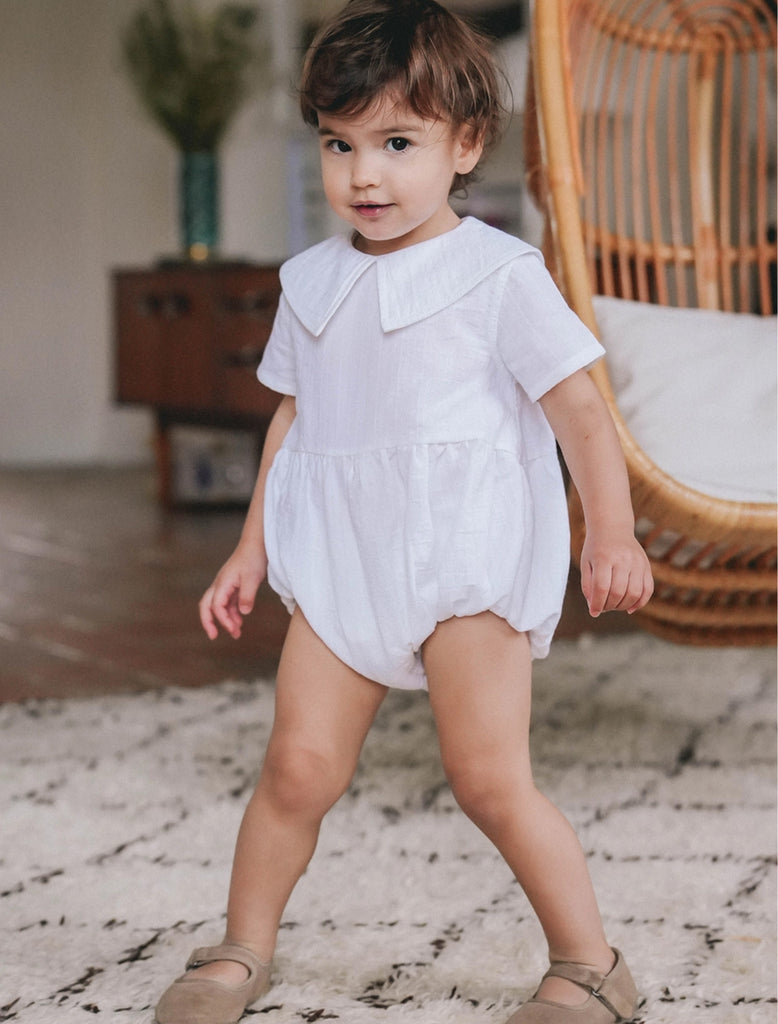 An image of a little girl wearing the Coco Romper in white.