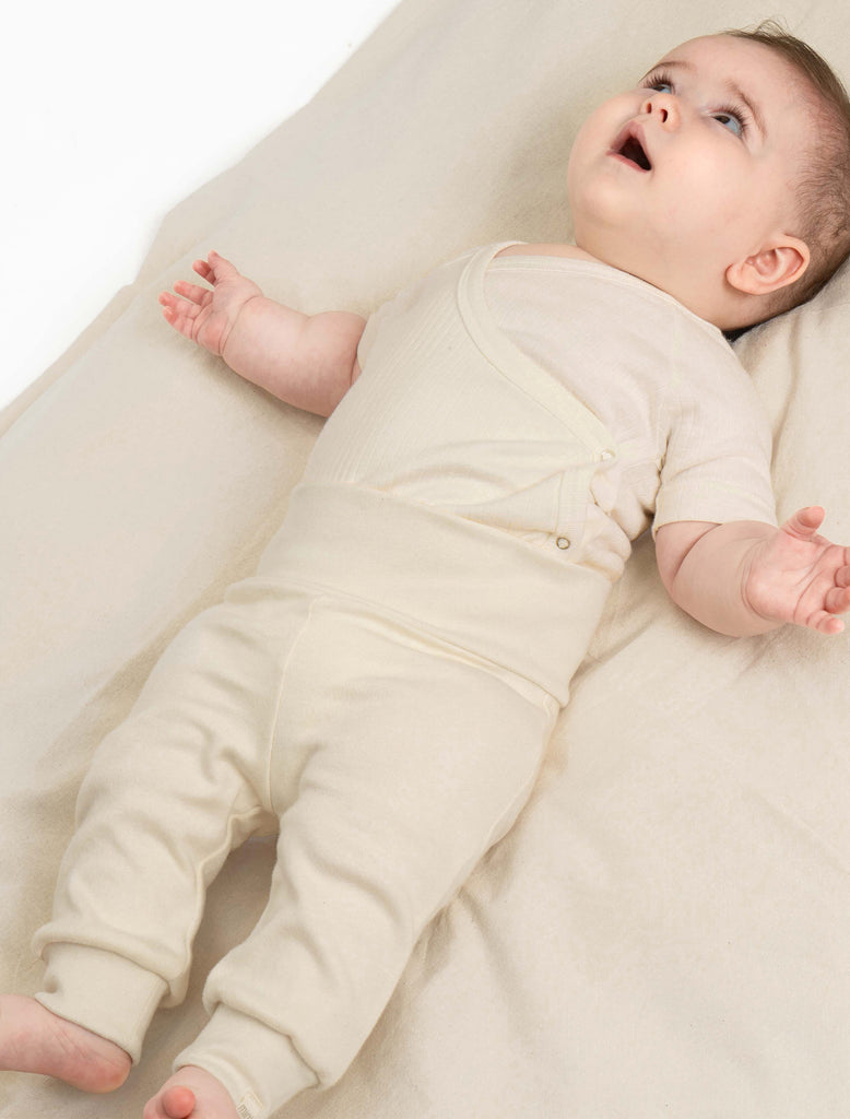 Image of a baby laying down wearing the cotton ribbed onesie and leggings in cream.