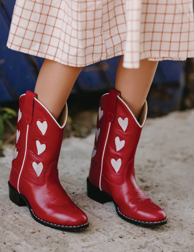 Red cowboy boots with heart patterns worn by a person on a blurred background