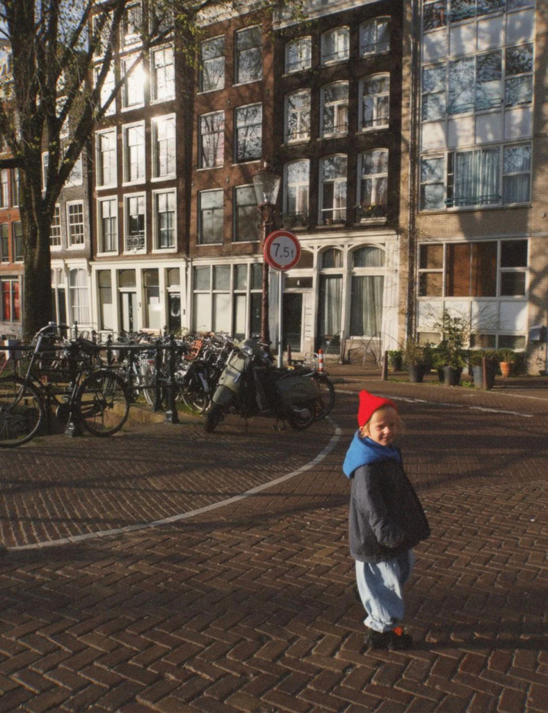Child standing on a cobblestone street in an urban setting with buildings and parked bicycles.