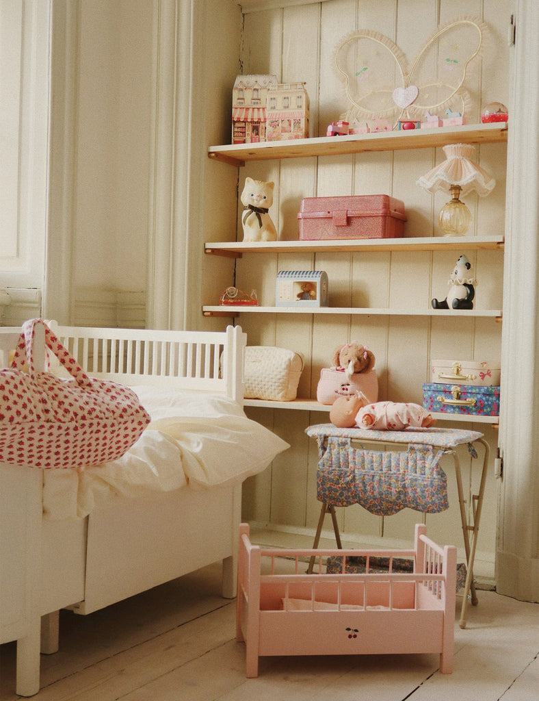 Nursery room with white crib, pink baby bed, and shelves with toys and decor.
