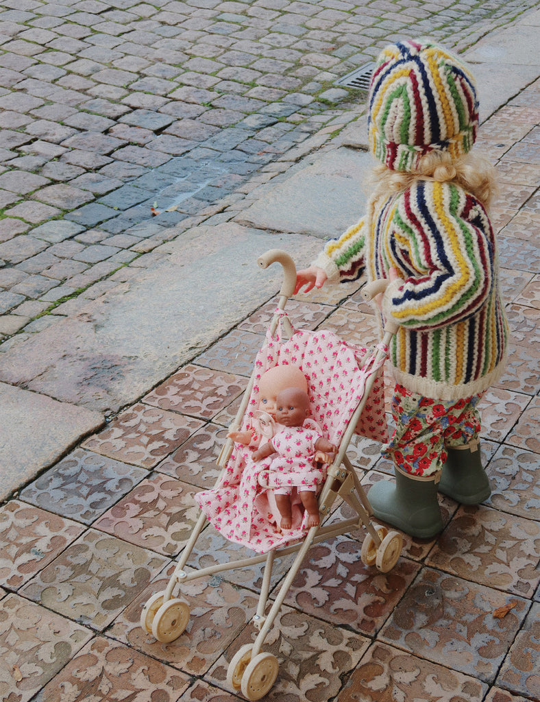 Child in colorful outfit pushing a doll in a stroller on a stone pavement