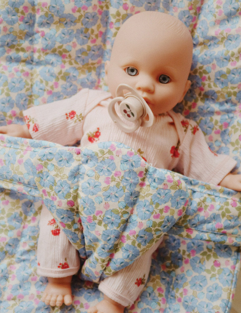 Baby doll with a pacifier lying on a floral blanket