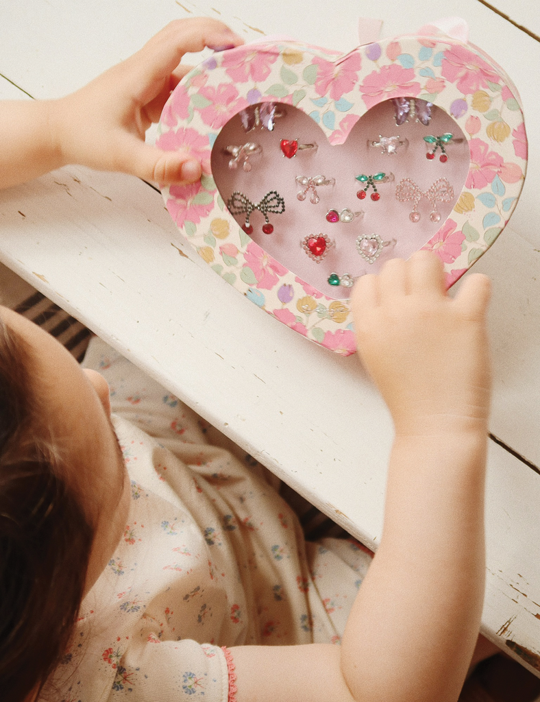 Child holding a heart-shaped box with decorative items on a wooden surface