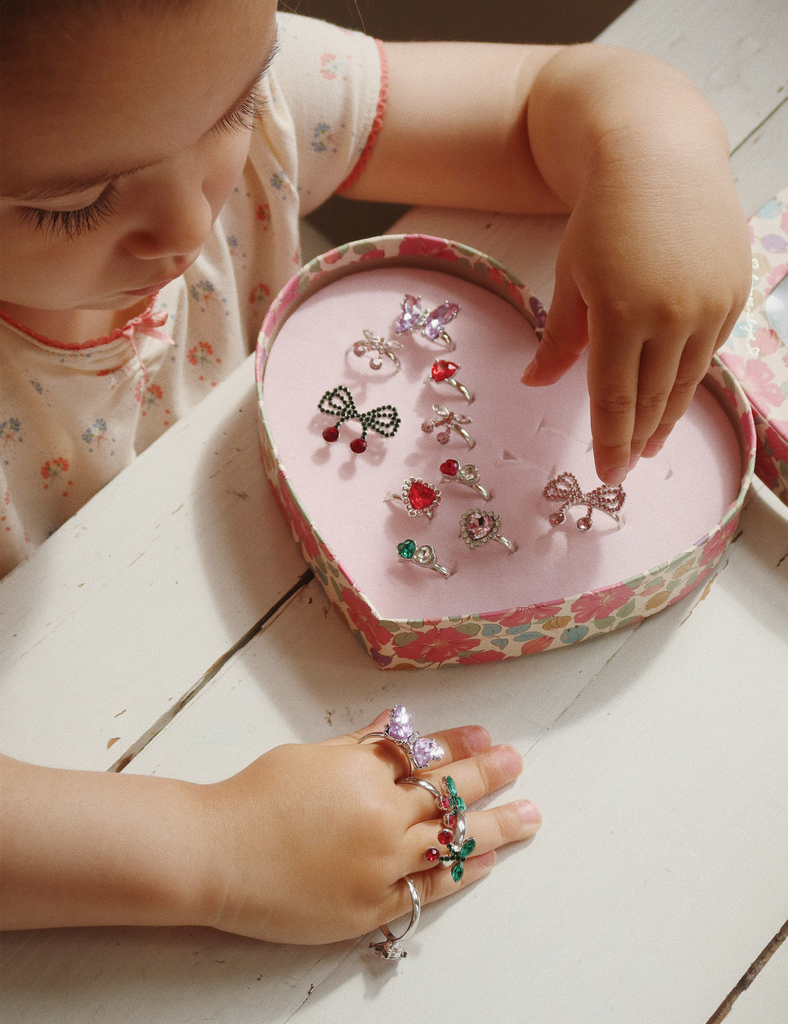 Child playing with decorative rings in a heart-shaped box on a wooden surface