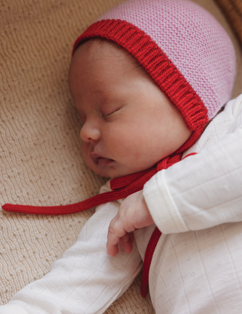 Newborn baby wearing a pink and red knitted hat on a beige surface