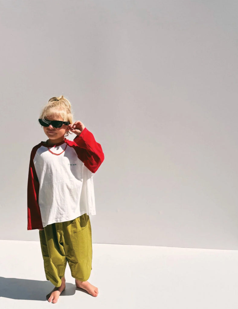 Child wearing a red and white shirt, green pants, and sunglasses on a plain background