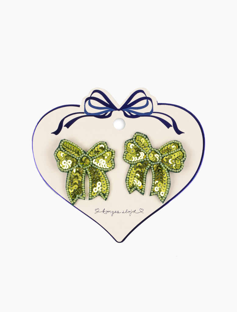 Green bow-shaped earrings on a heart-shaped card with a blue ribbon.