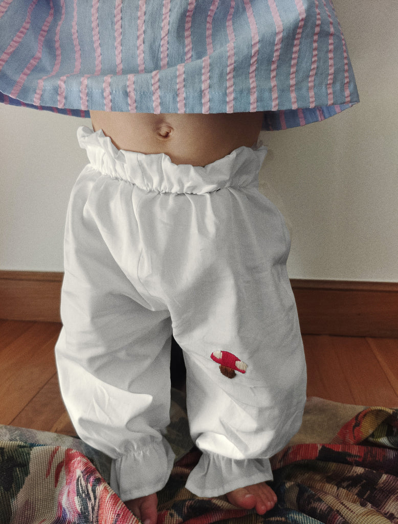 Child wearing a striped hat and white pants with a red design on a wooden floor.