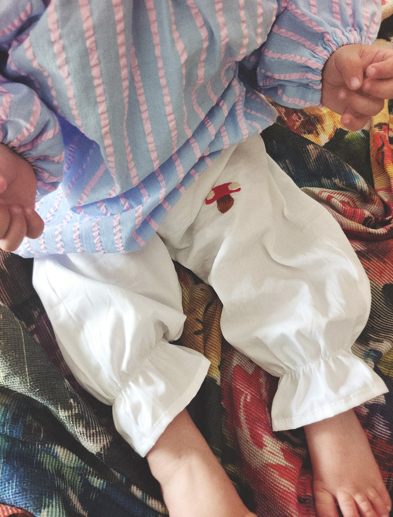 Close-up of a child's legs wearing white pants with a red heart design, sitting on a colorful surface.