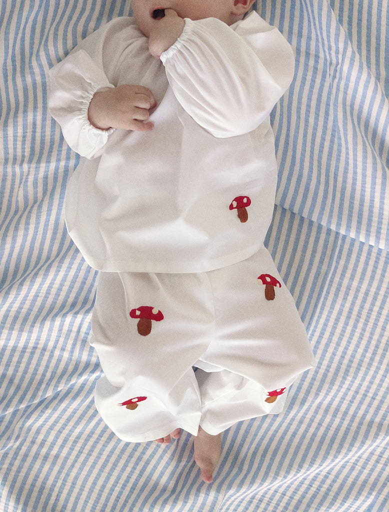 Baby wearing a white outfit with red mushroom designs on a blue and white striped background
