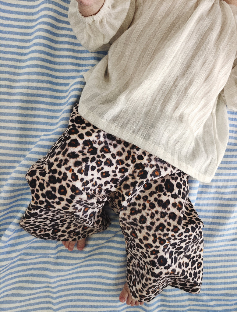 Baby wearing leopard print pants and a light-colored top on a blue and white striped fabric background