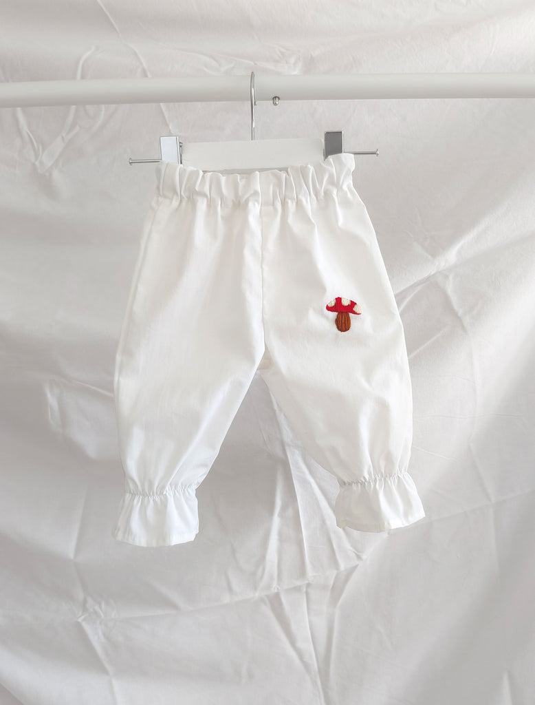 White pants with a red flower design hanging on a white background