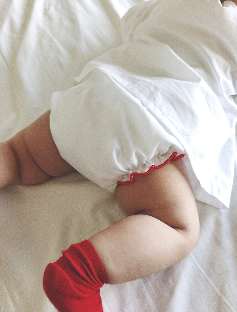 Child's wearing a white shirt with red trim and red socks on a white background