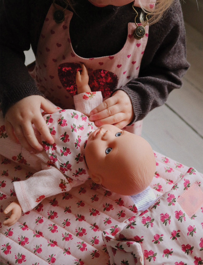 Child holding a doll with a floral dress, wearing a matching apron.