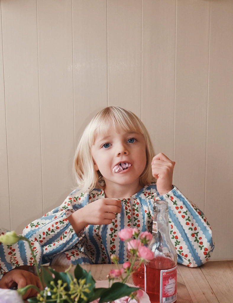 Child sitting at a table with flowers and a bottle, against a wooden panel background