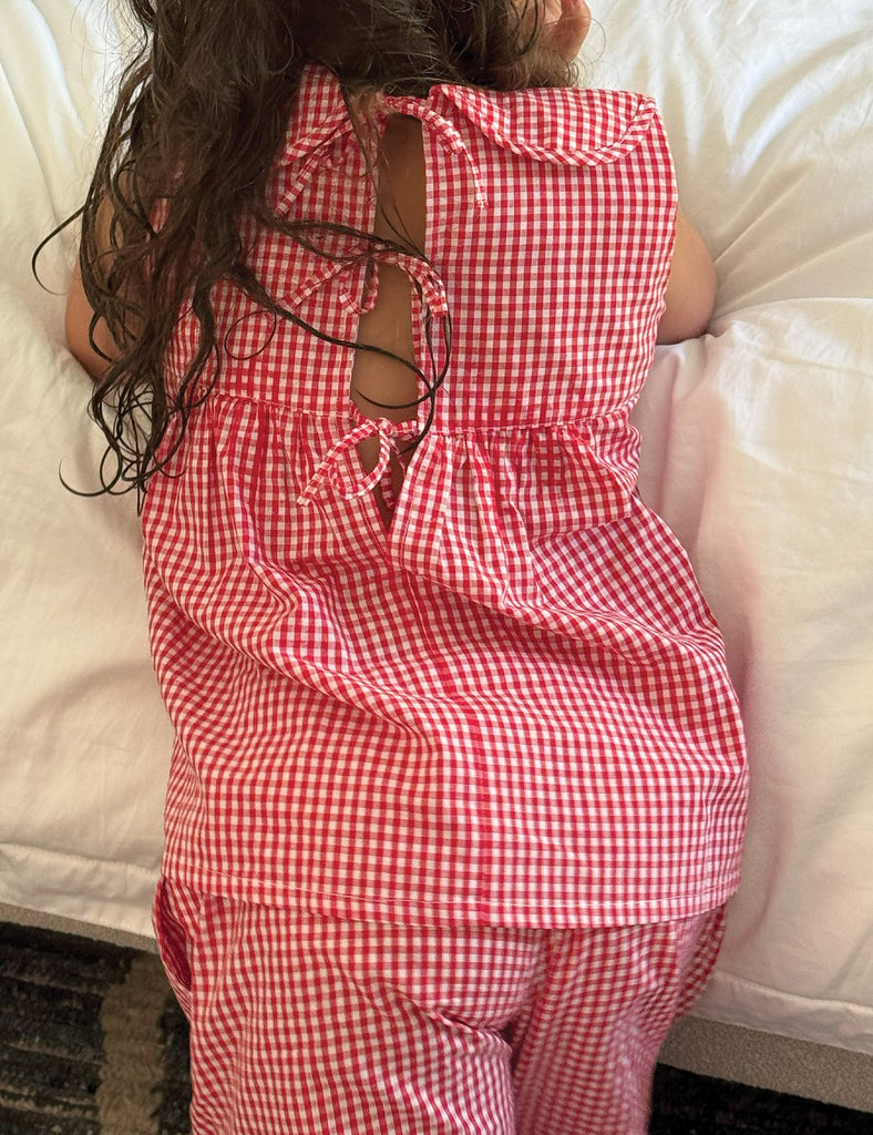 Child wearing a red and white checkered outfit on a bed
