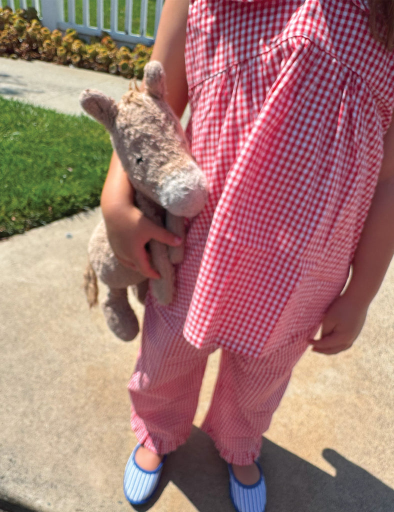Little girl wearing red and white checkered top and pants holding a stuffed pony on a sidewalk.