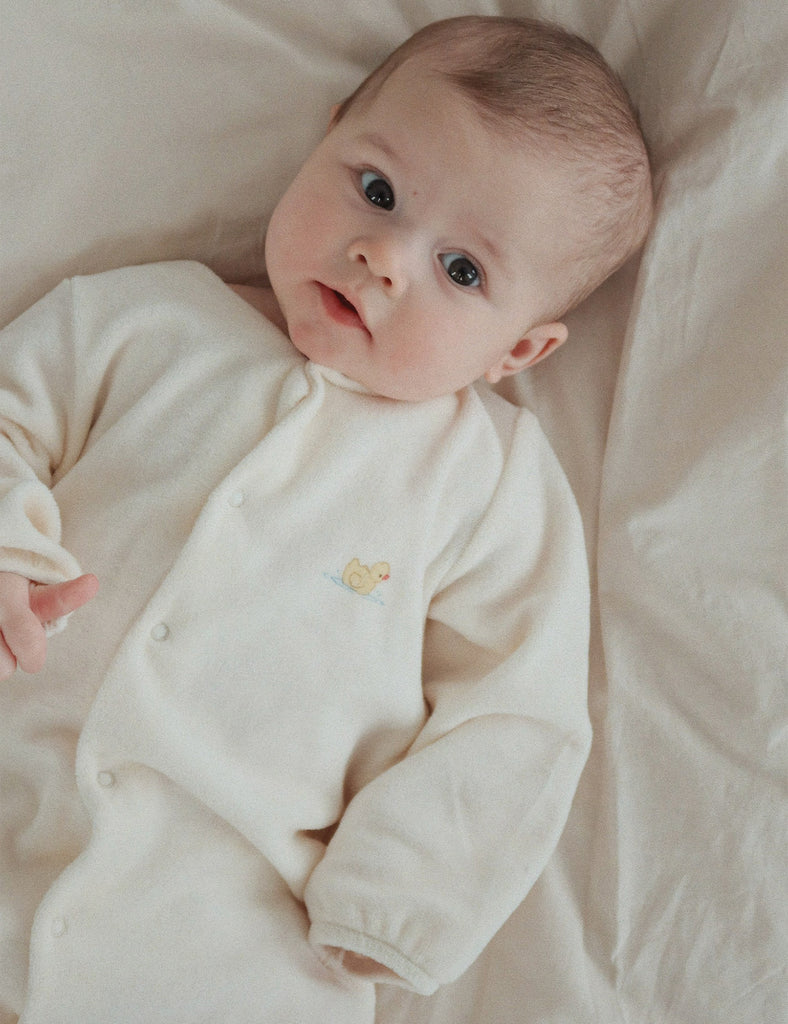 Baby wearing a white onesie with a small design, lying on a soft surface.