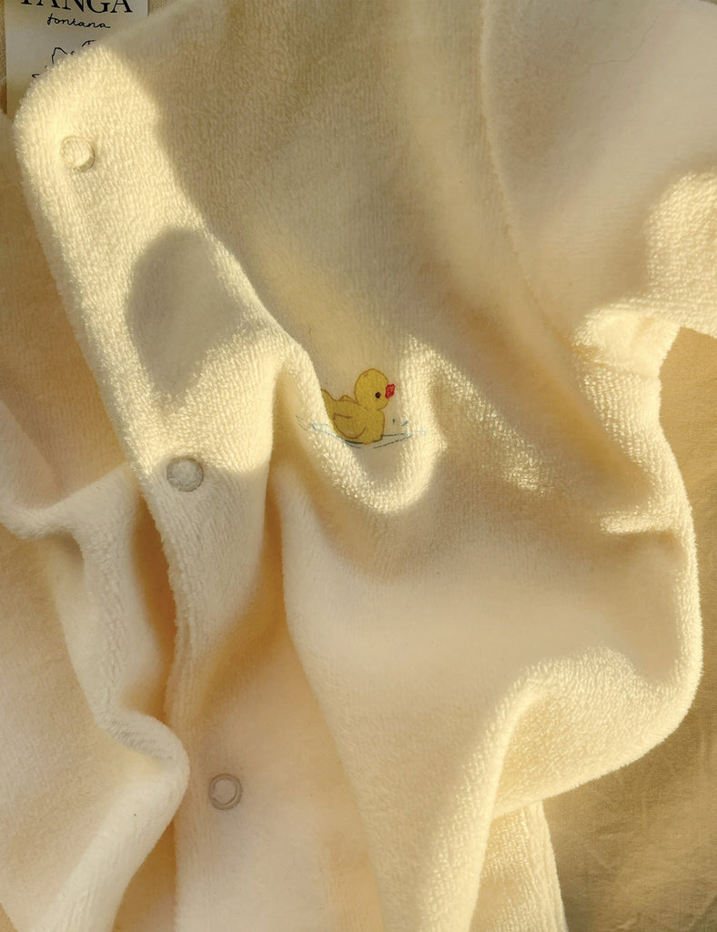 Close-up of a soft, beige fabric with a small yellow duck design and buttons.