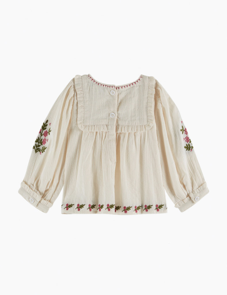 Beige blouse with floral embroidery on sleeves and hem against a white background