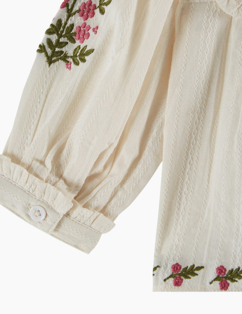 Close-up of a cream-colored garment with floral embroidery on a white background