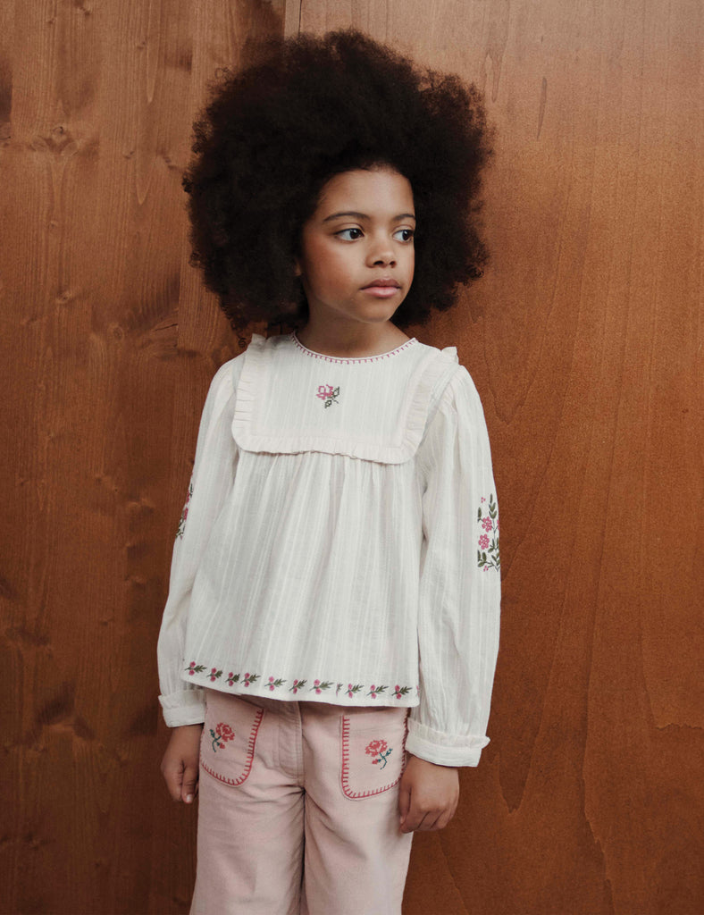Young girl wearing a white blouse with floral embroidery against a wooden background