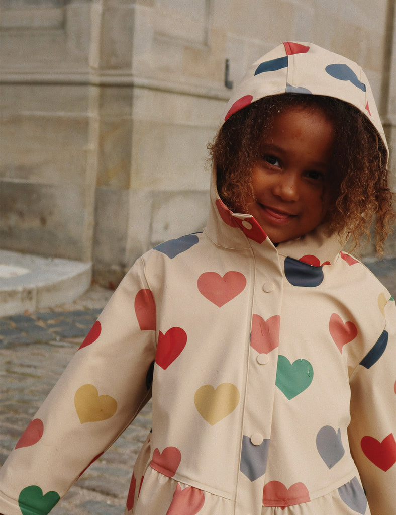 Child wearing a raincoat with colorful heart patterns outdoors.