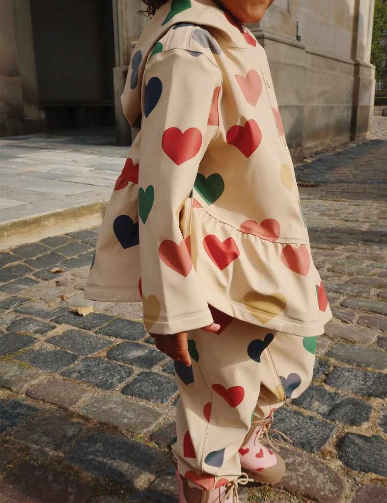 Person wearing a beige outfit with colorful heart patterns on a cobblestone street.