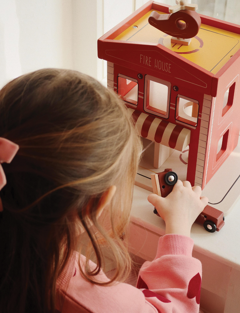 Child playing with a wooden toy firehouse set