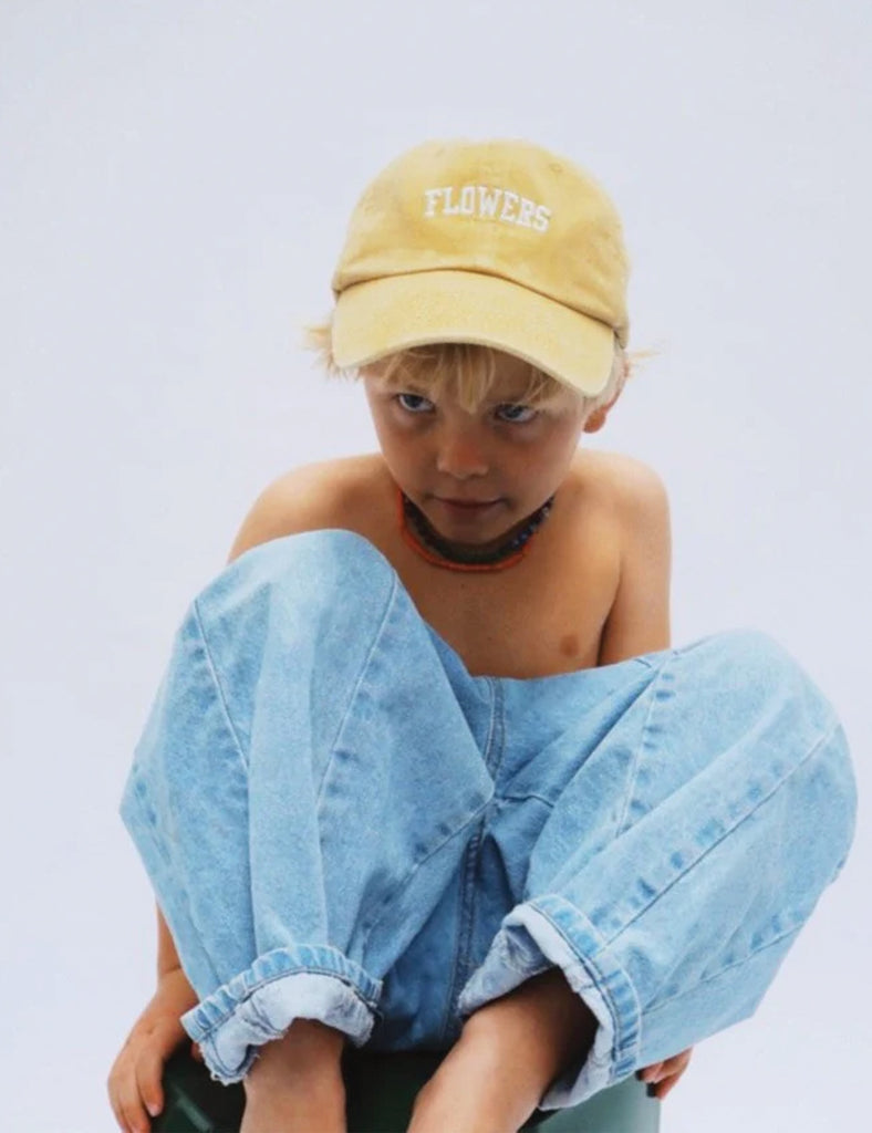 Person wearing a yellow 'FLOWERS' cap and light blue jeans on a white background