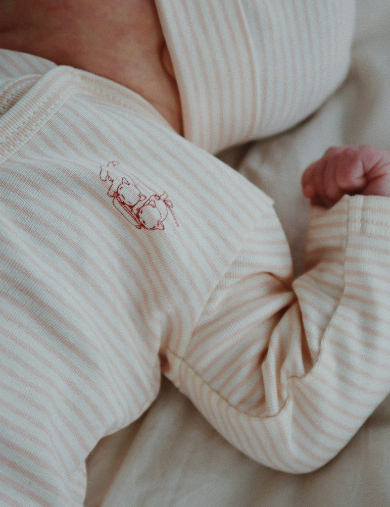 Close-up of a baby's hand and foot in striped pajamas with a small embroidered design.