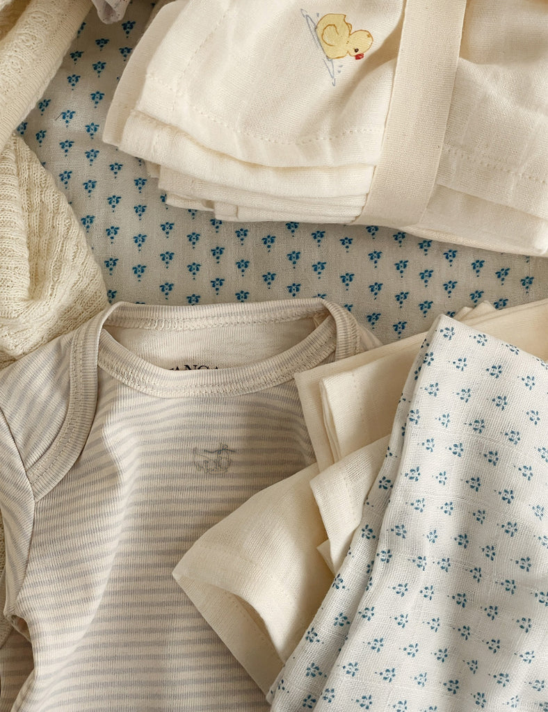 Stack of baby clothes including a onesie and pants on a floral-patterned surface.