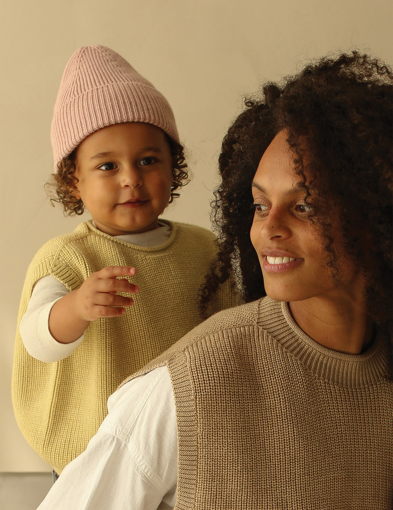 Image of a child wearing a pink knit beanie and yellow knitted vest.
