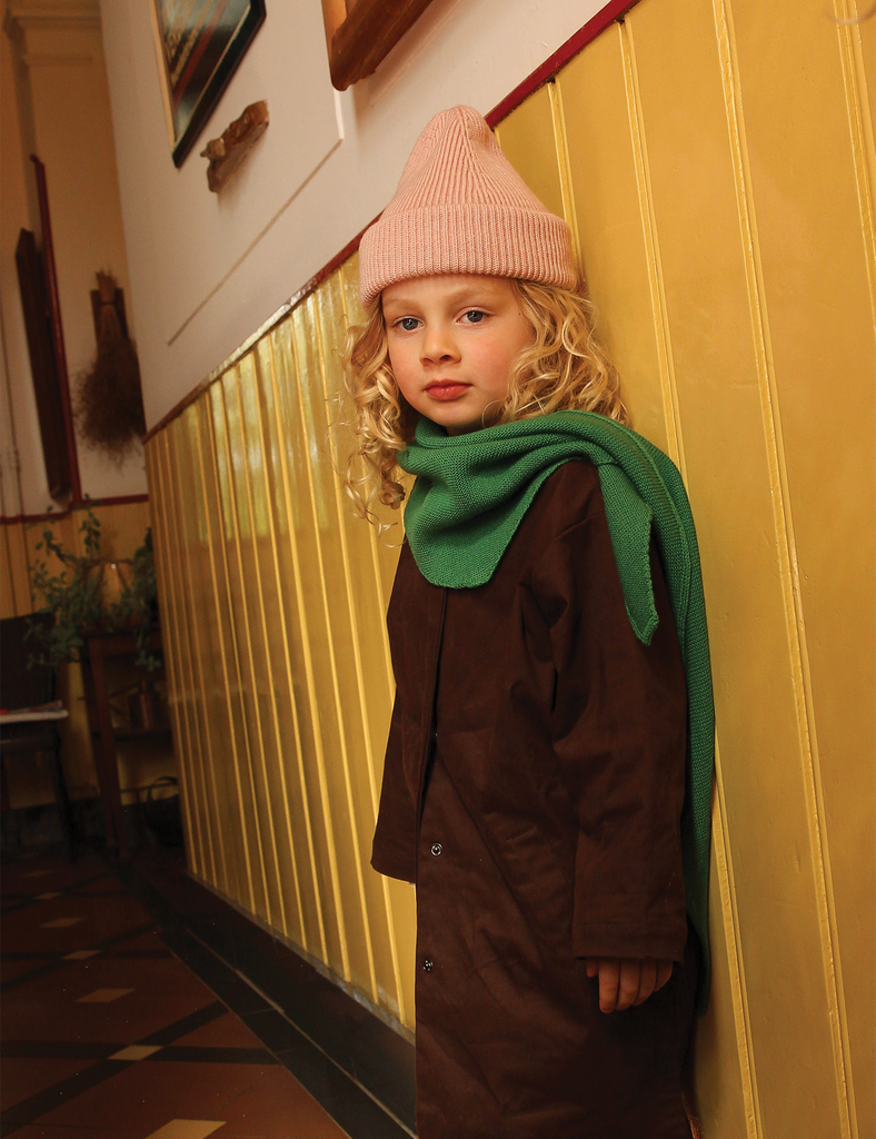 Image of a child wearing a pink knitted beanie standing in front of a yellow wall.