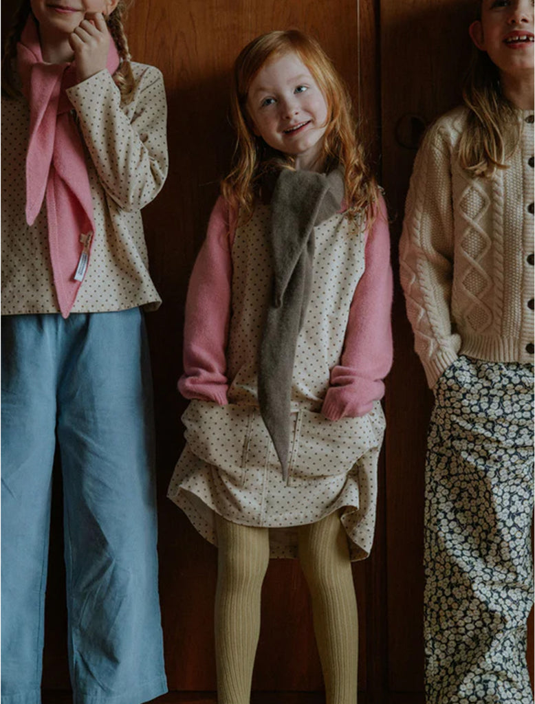 Three children standing close together against a wooden wall.