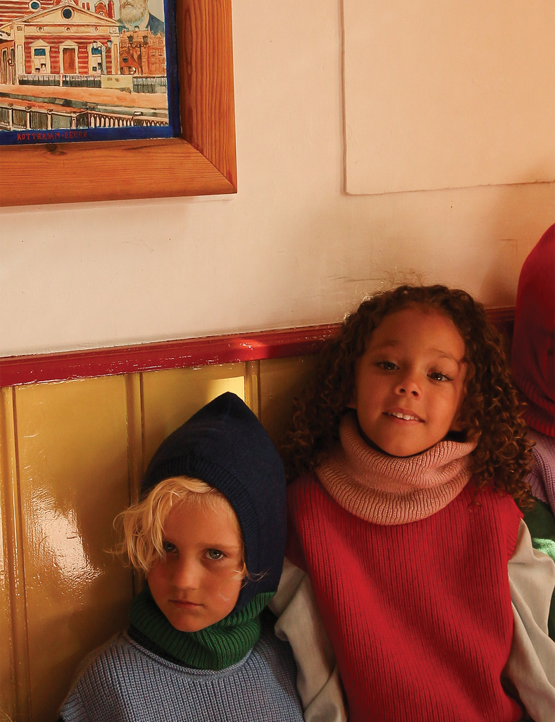 Two children sitting against a wall with a framed picture above them.