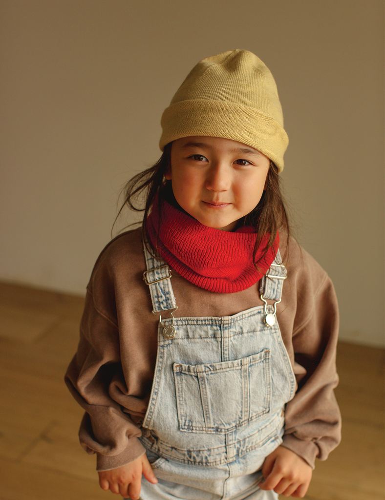 Child wearing a red knitted scarf and yellow beanie.