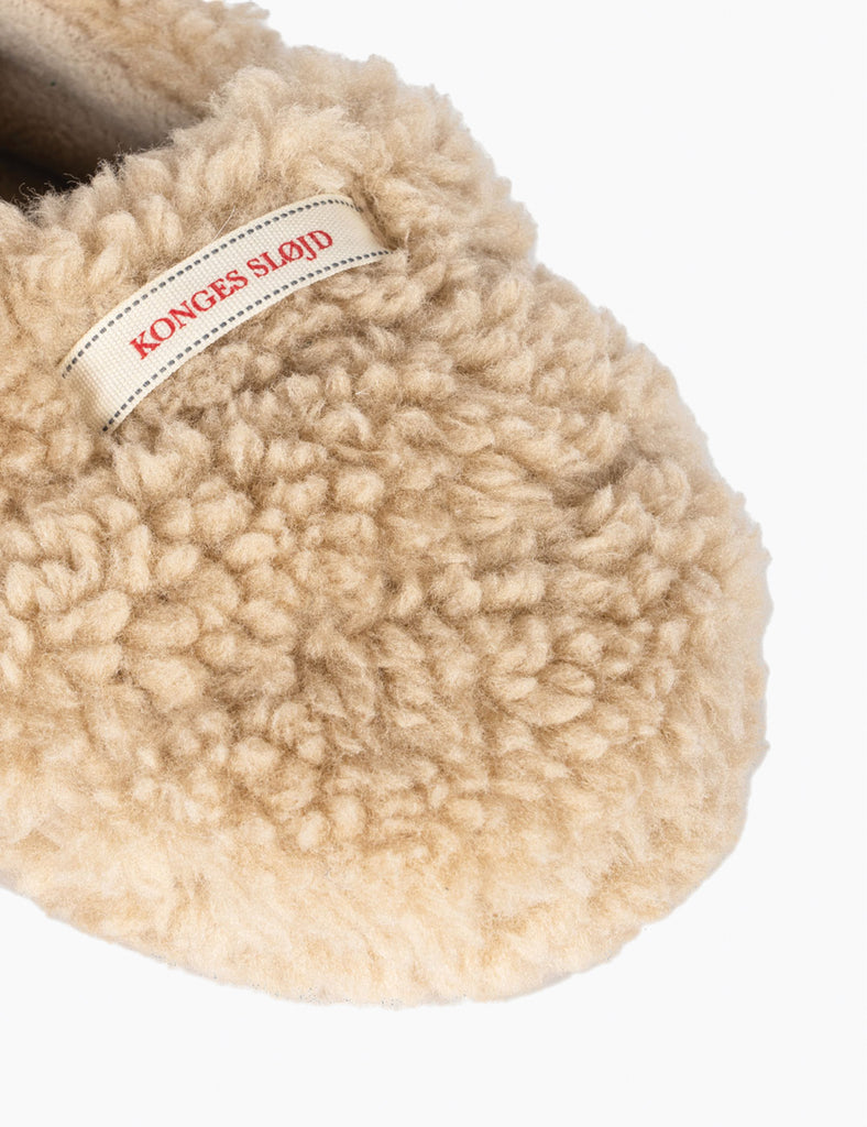 Beige fuzzy slipper with a visible brand label on a white background