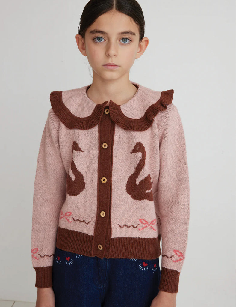 Young girl wearing a pink sweater with swan design on a plain background
