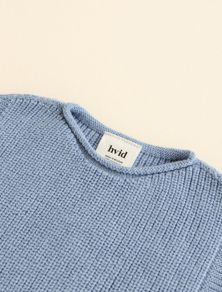 Close up image of a blue knitted baby vest showing the back label branding.