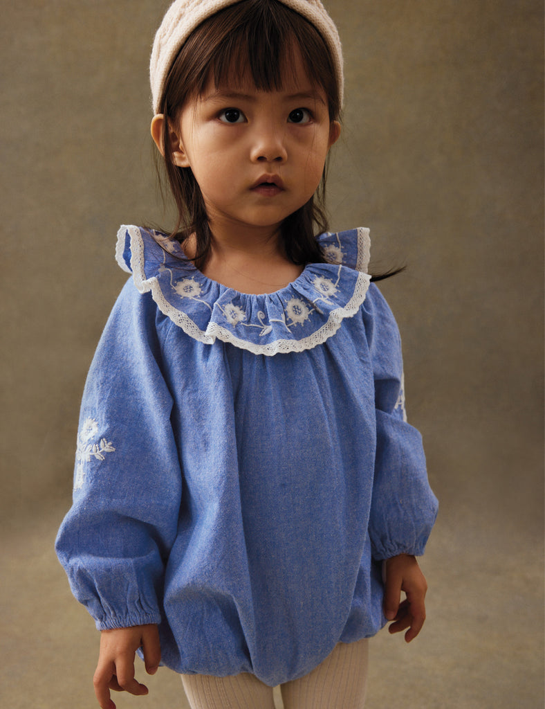 Child wearing a blue blouse with lace collar against a brown background