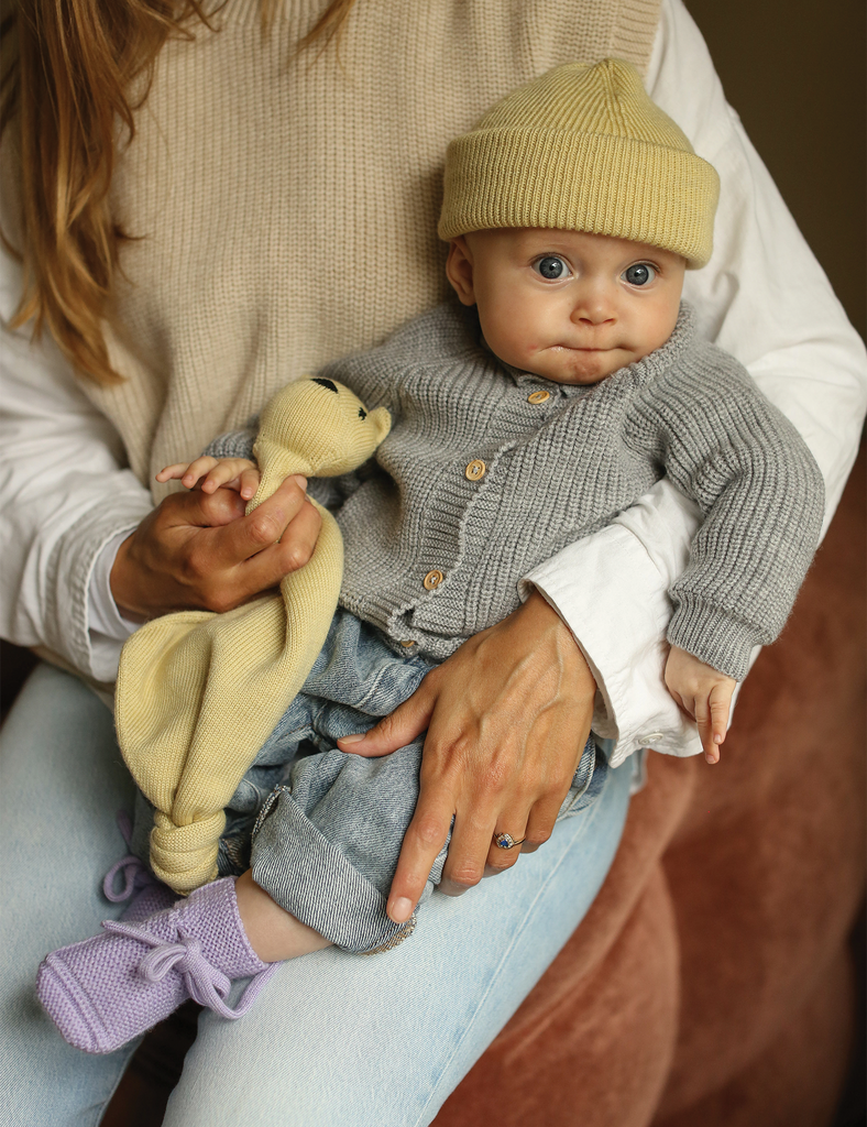 Baby in a gray outfit with a yellow hat being held by an adult