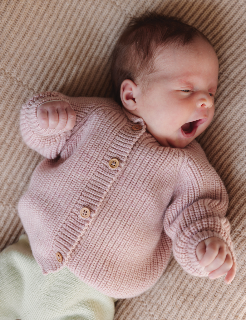 Newborn baby wearing a pink knitted sweater on a beige blanket
